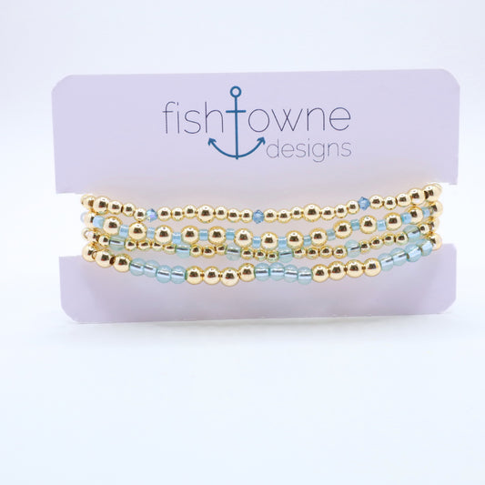 Three-piece sky blue hematite bracelet stack featuring gold-tone beads and translucent blue glass accents.