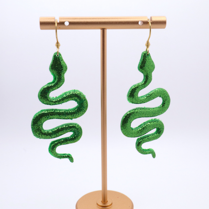 Green snake-shaped earrings on a gold stand against a white background