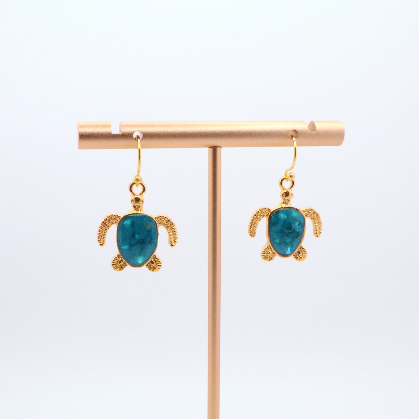 Tortoise-shaped earrings with turquoise resin on a gold earring stand against a white background