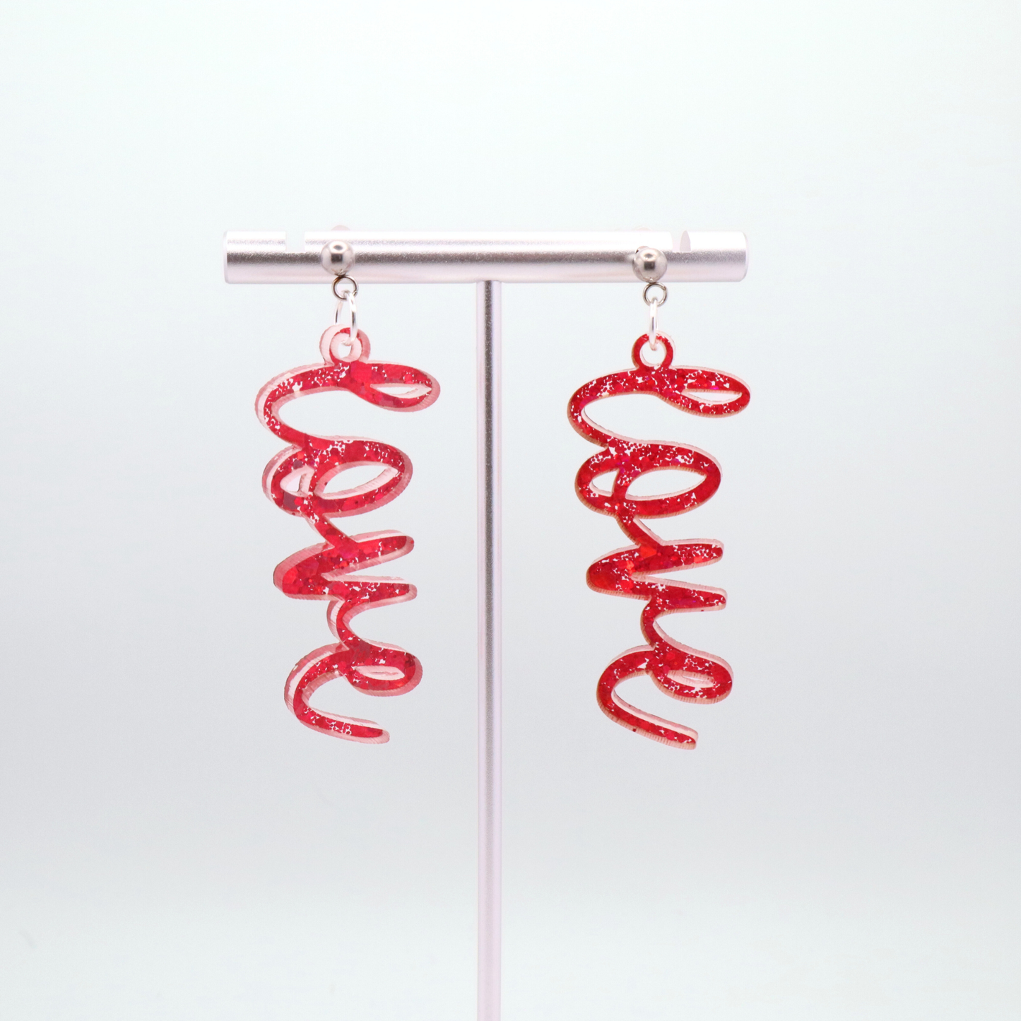 Pink glitter 'love' earrings on a white gray background