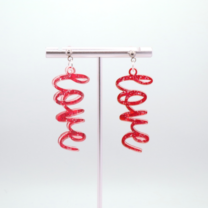 Pink glitter 'love' earrings on a white gray background