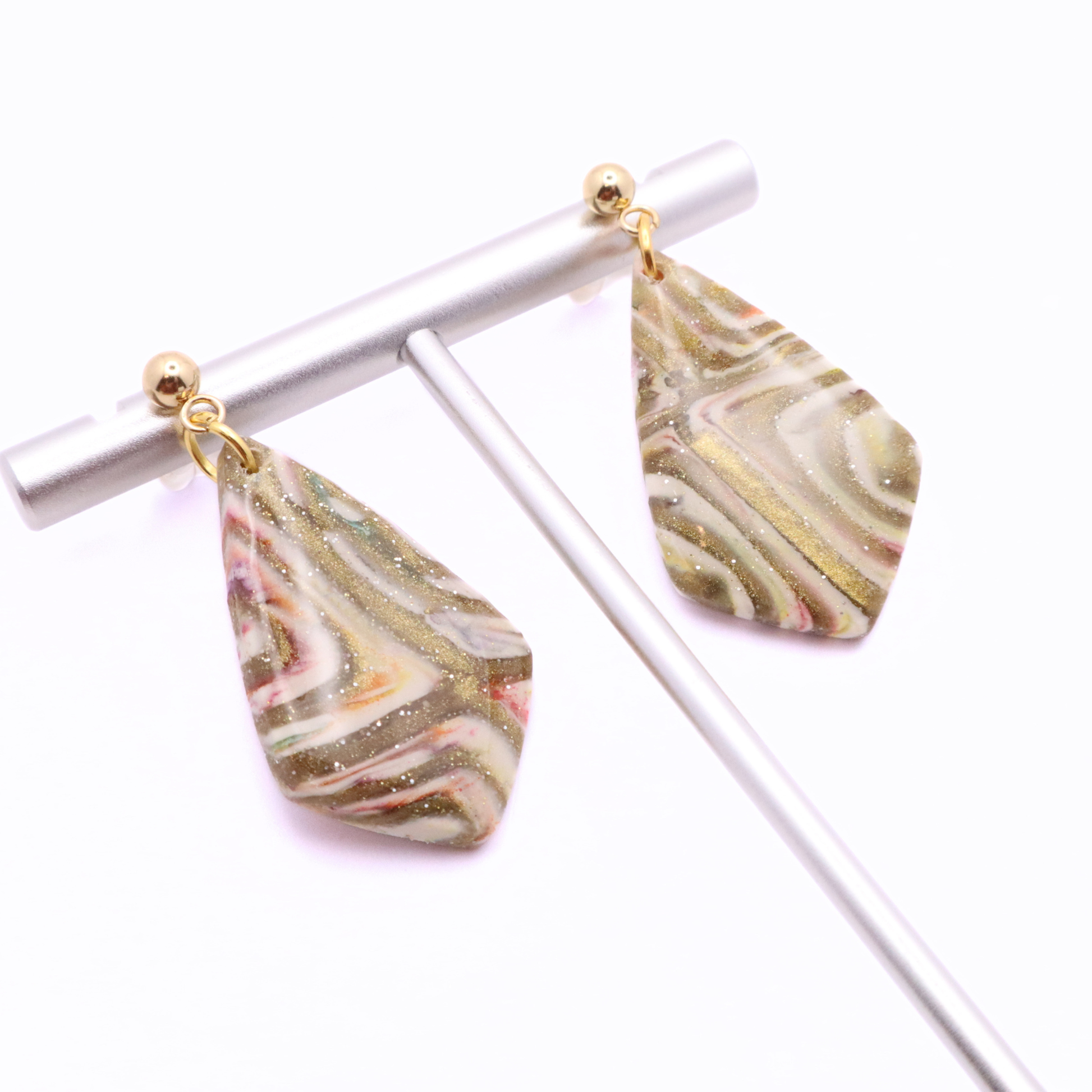 Lightweight polymer clay dangle earrings with abstract swirl pattern and gold shimmer, hanging from stainless steel posts on display bar