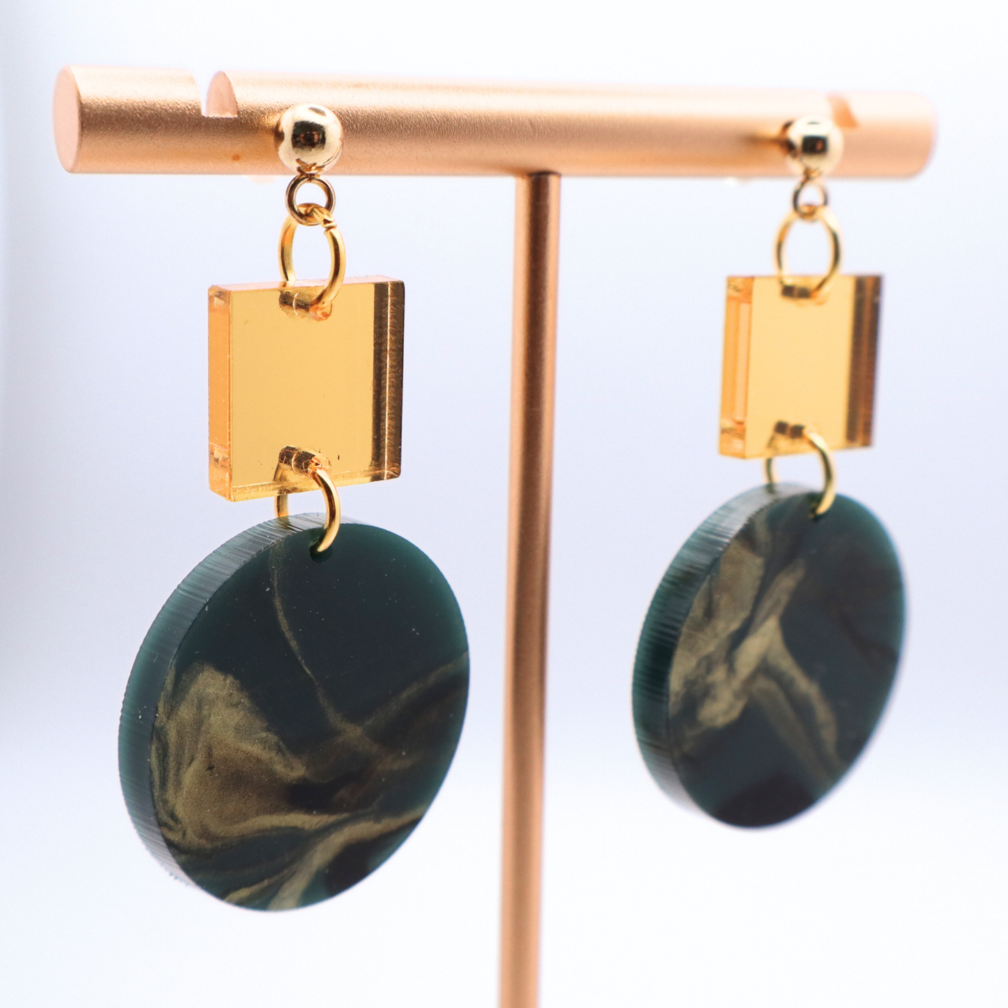 Gold and green marbled earrings on a display stand against a white background