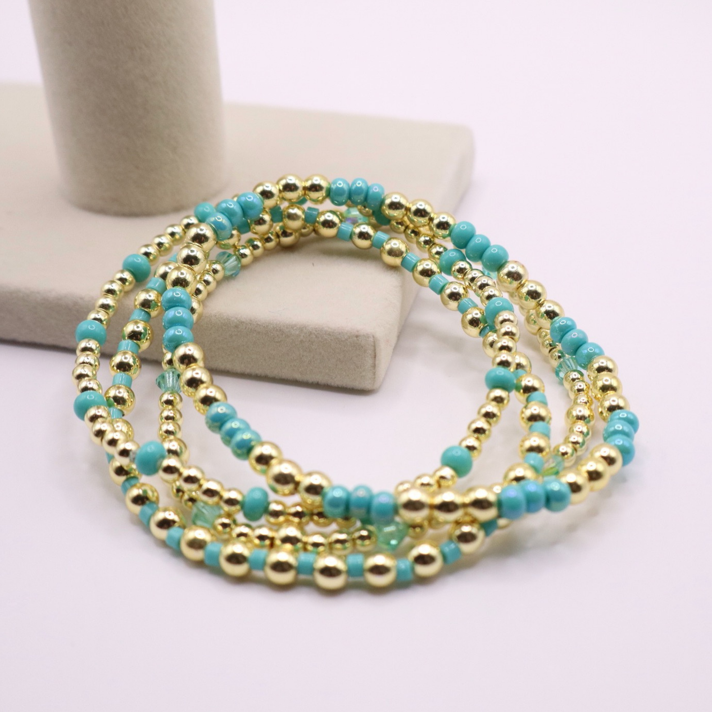 Layered bracelet stack with turquoise Preciosa seed beads, shimmering crystal accents, and gold-tone hematite beads on a clean white background.