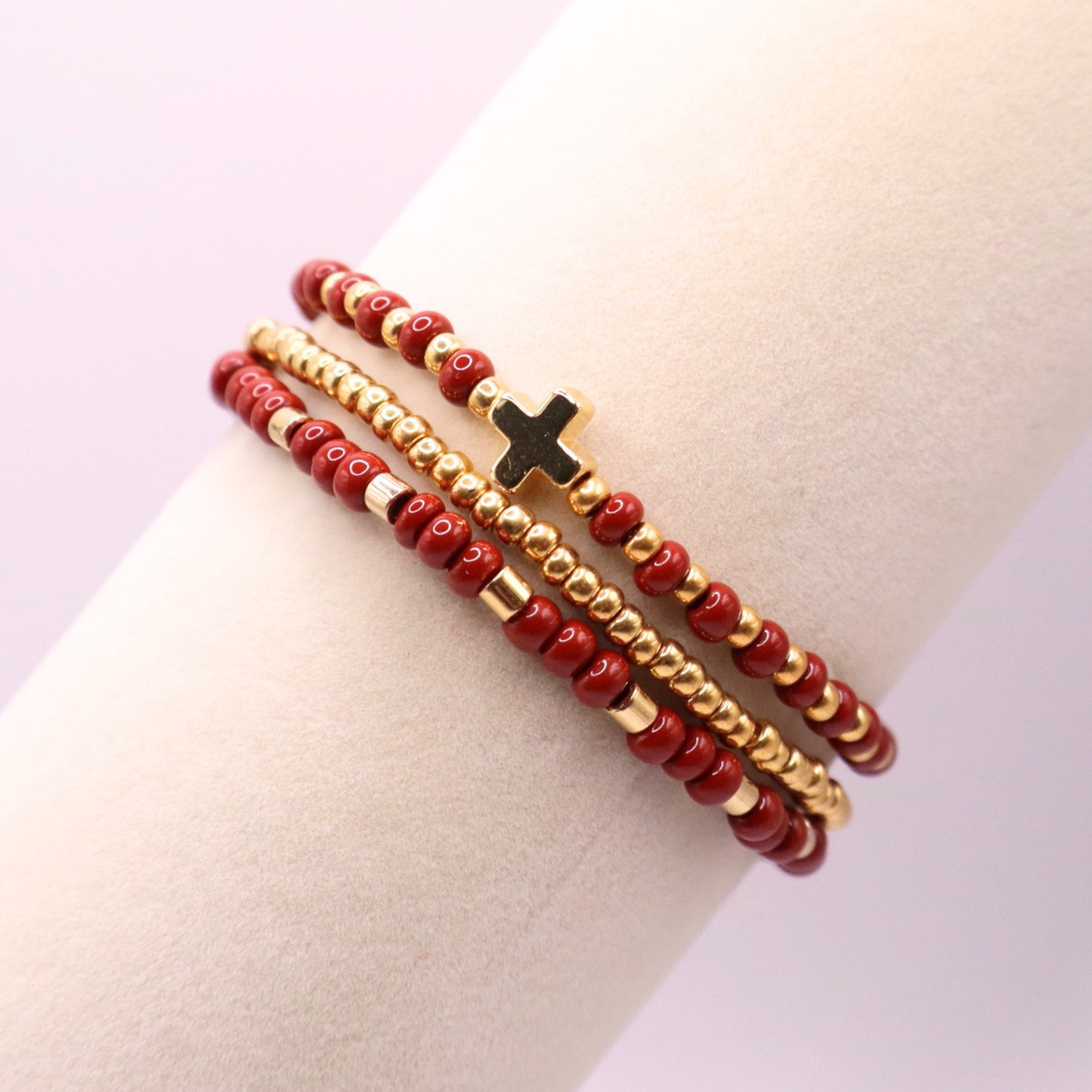 A rust and gold bracelet stack featuring three bracelets. One all gold, and one with a gold cross centerpiece charm.