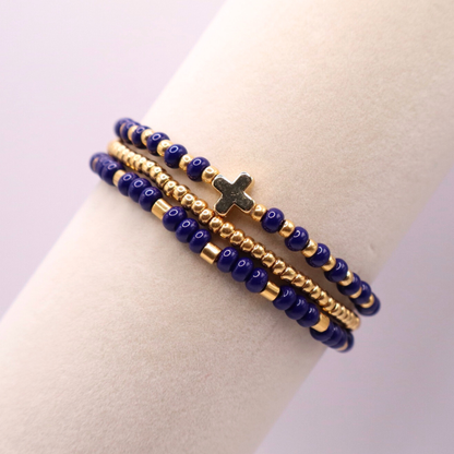 Three beaded bracelets with navy blue and gold accents and a cross charm on a light background