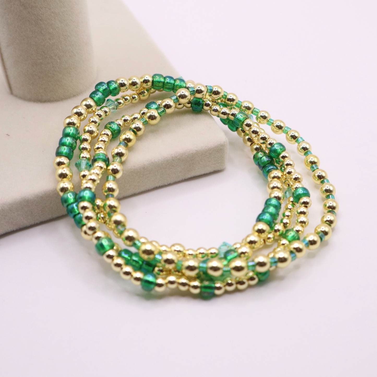 Handmade bracelet stack with green Preciosa seed beads, iridescent crystal accents, and polished gold-tone hematite beads on a clean white background.