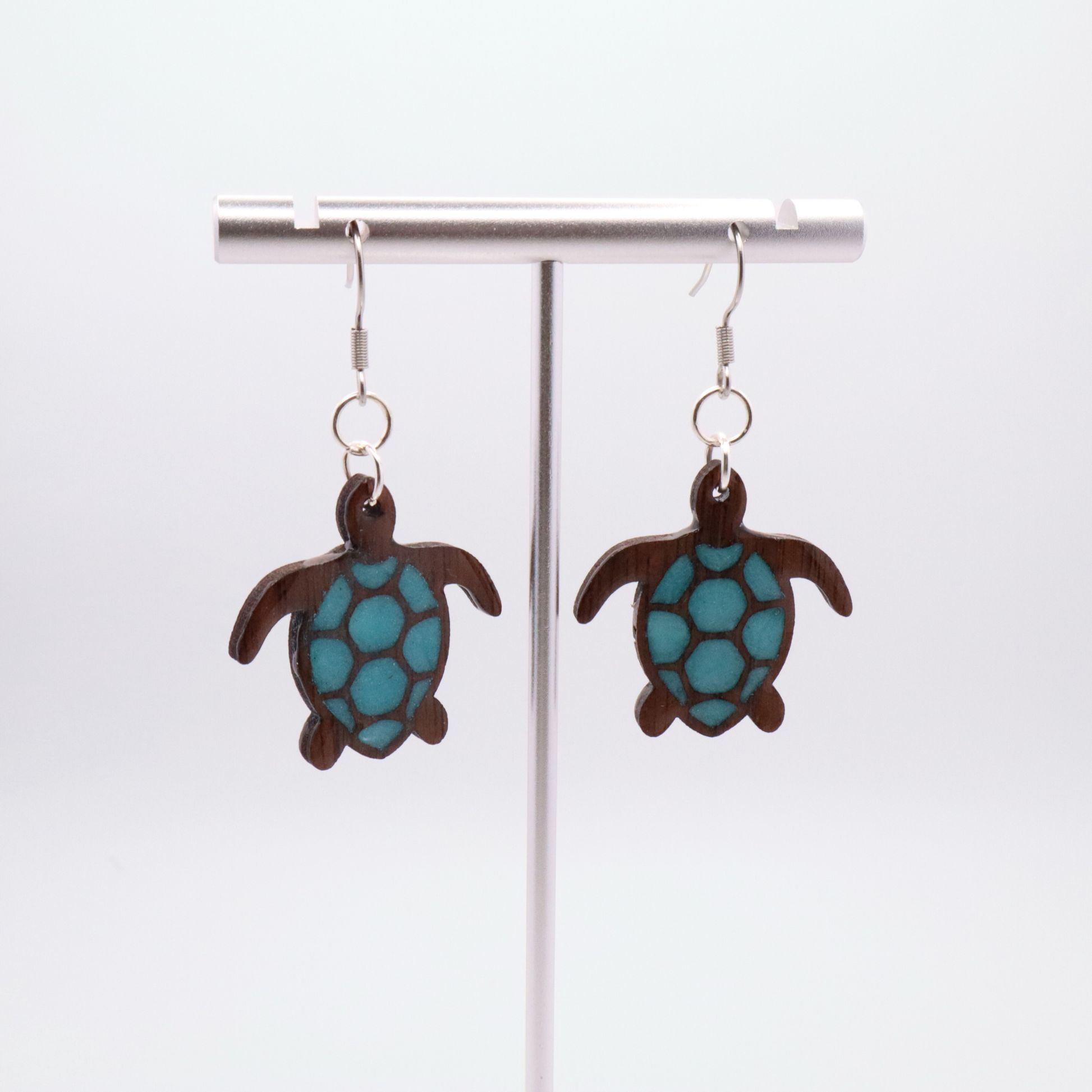 Turtle-shaped black walnut earrings with sea glass blue resin on a white background