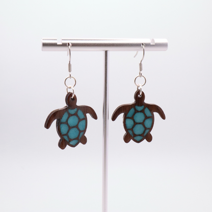Turtle-shaped black walnut earrings with sea glass blue resin on a white background