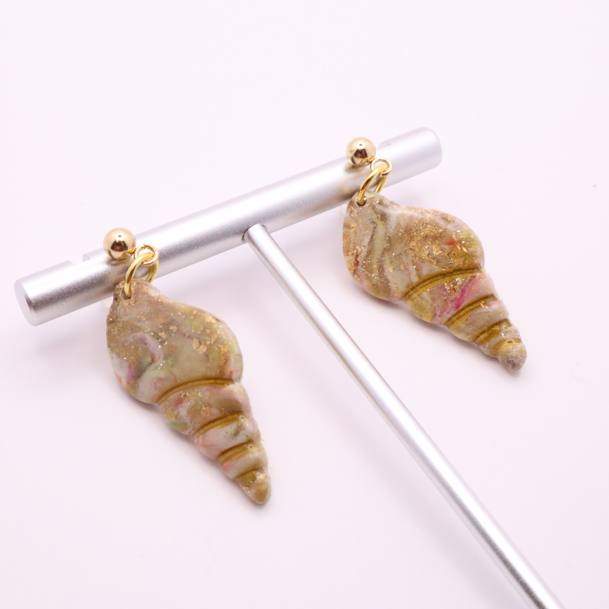 Seashell drop earrings with gold stud tops displayed on a minimalist jewelry stand