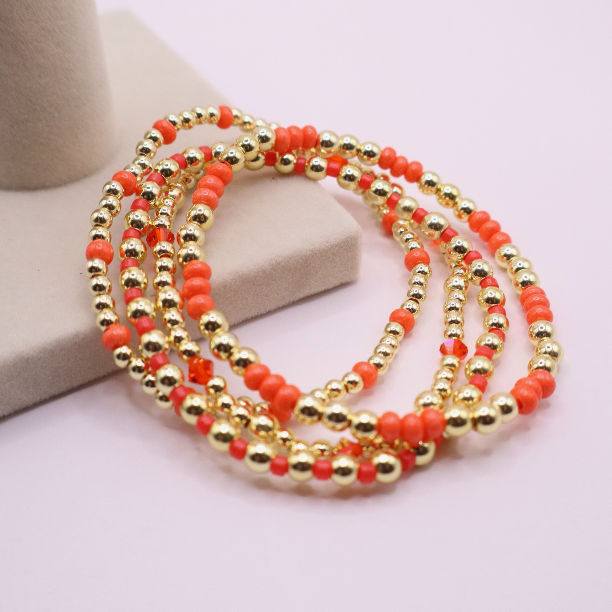 Stack of handmade stretch bracelets featuring vibrant coral Preciosa seed beads, faceted crystal accents, and polished gold-tone hematite beads on a clean white background.