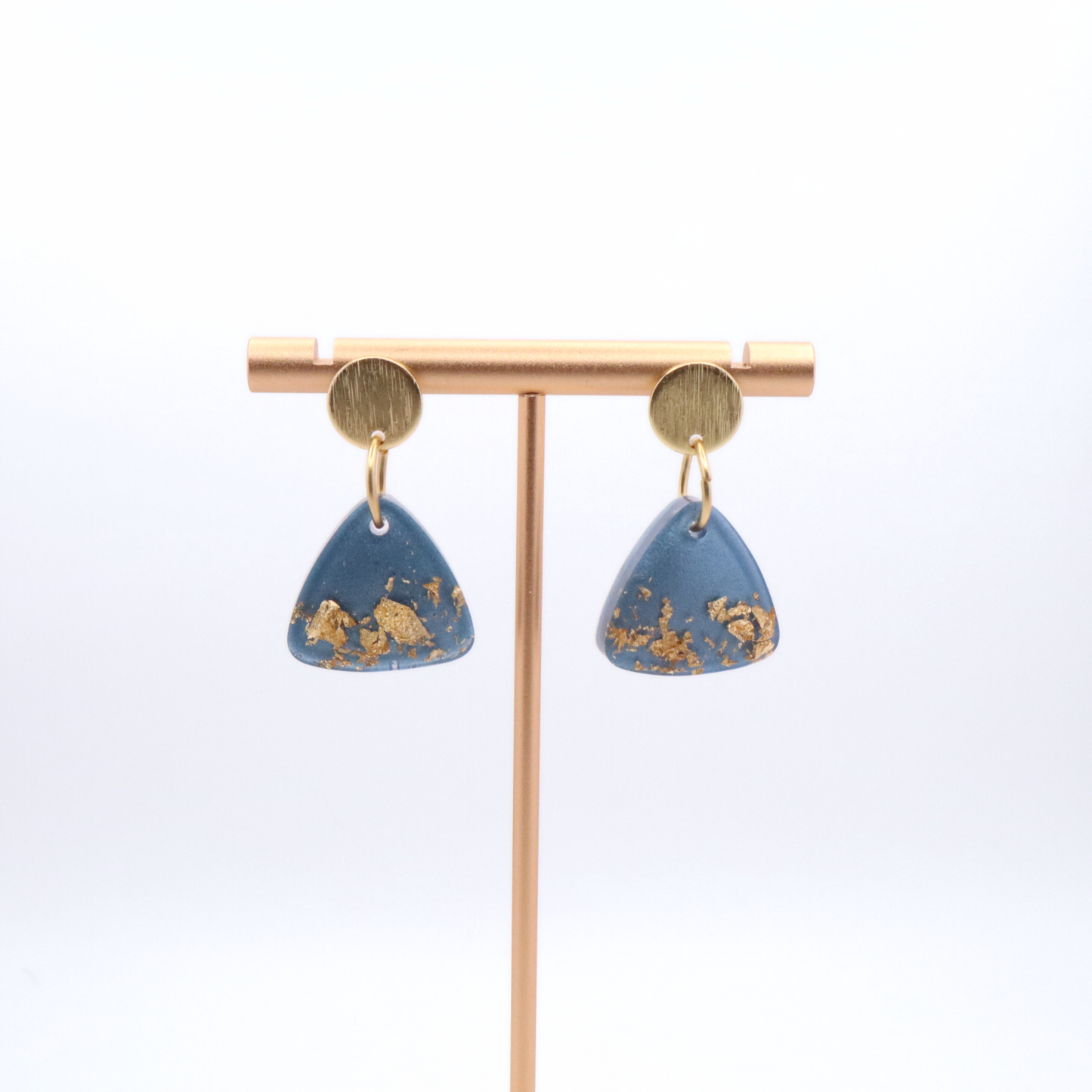 Blue earrings with gold accents on a gold stand against a white background
