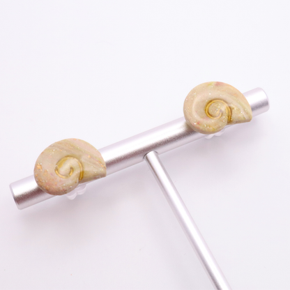 Small shell-shaped stud earrings with gold swirl center displayed on a minimalist stand