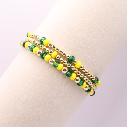 Three beaded bracelets in gold, green, and yellow on a person's wrist against a light background