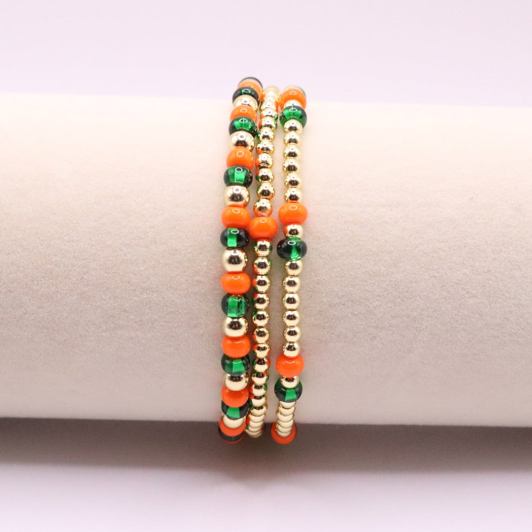 Three orange, green, and gold beaded bracelets on a display