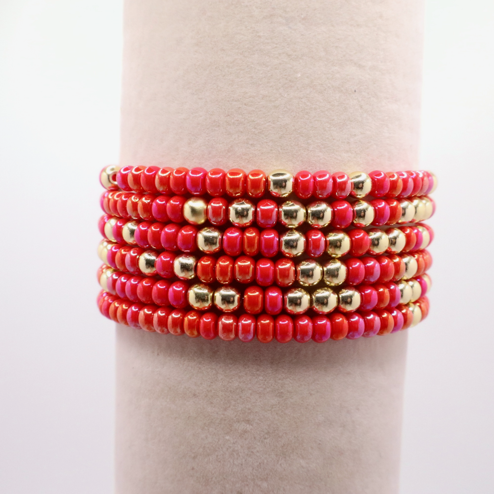 Stack of six pink and gold beaded bracelets on a neutral background