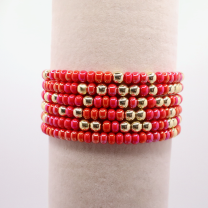Stack of six pink and gold beaded bracelets on a neutral background