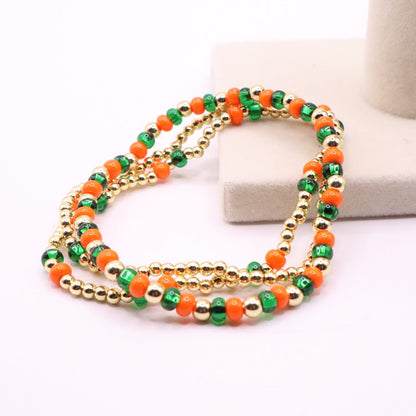 Three orange, green, and gold bracelets laying on a light background
