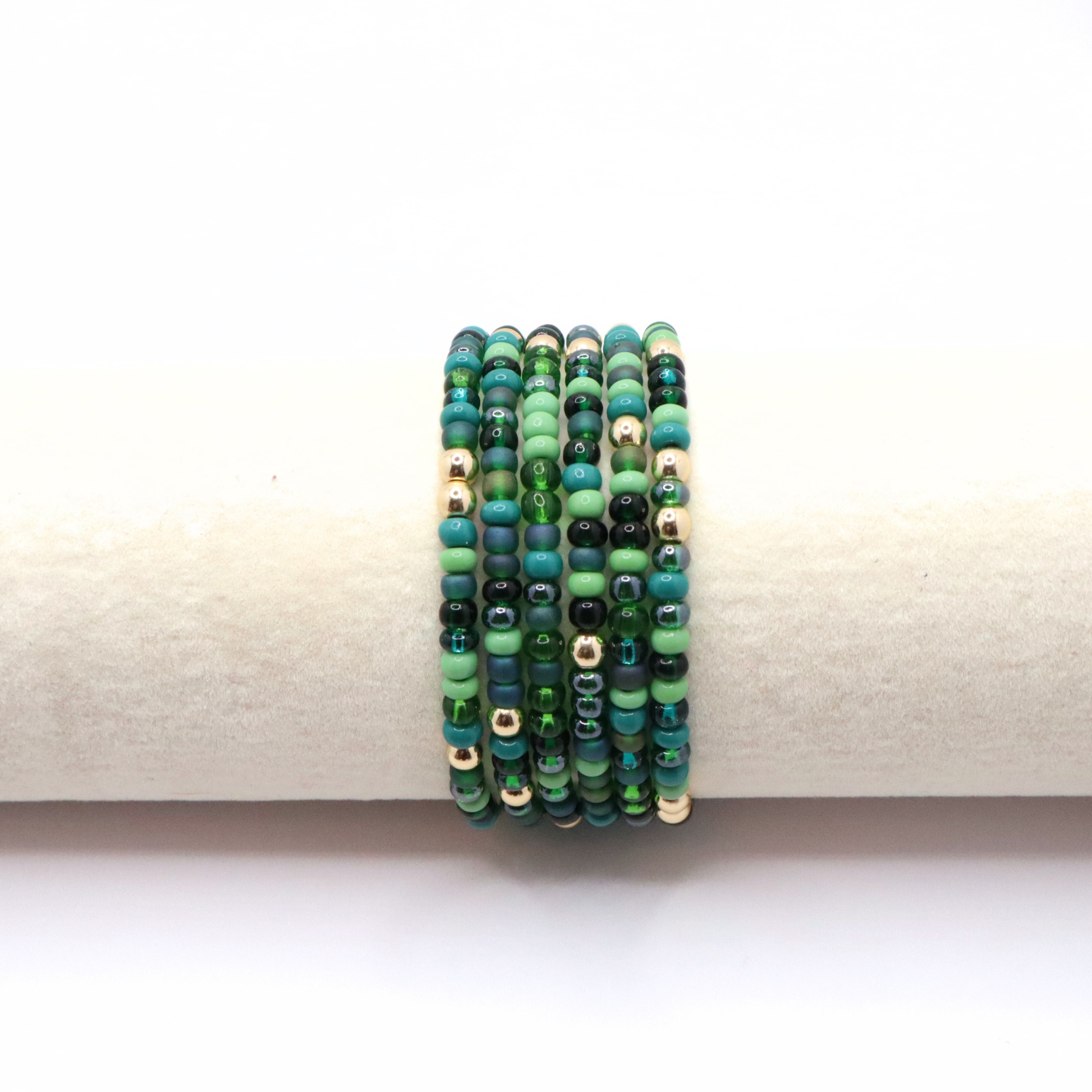 Set of six green beaded bracelets on a white background