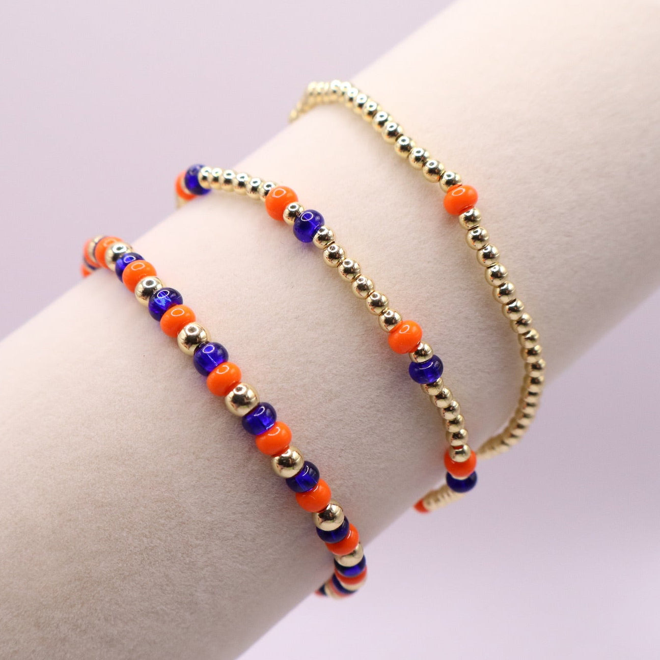 Three orange blue and gold bracelets on a bracelet display against a light background
