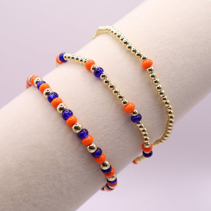 Three orange blue and gold bracelets on a bracelet display against a light background