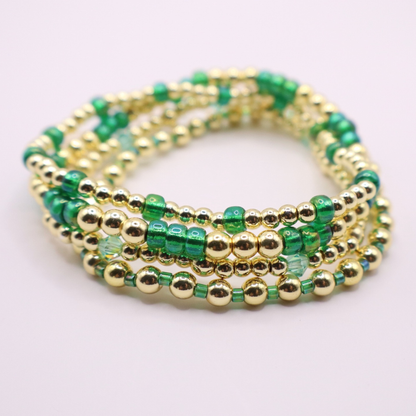 Handmade bracelet stack with green Preciosa seed beads, iridescent crystal accents, and polished gold-tone hematite beads on a clean white background.
