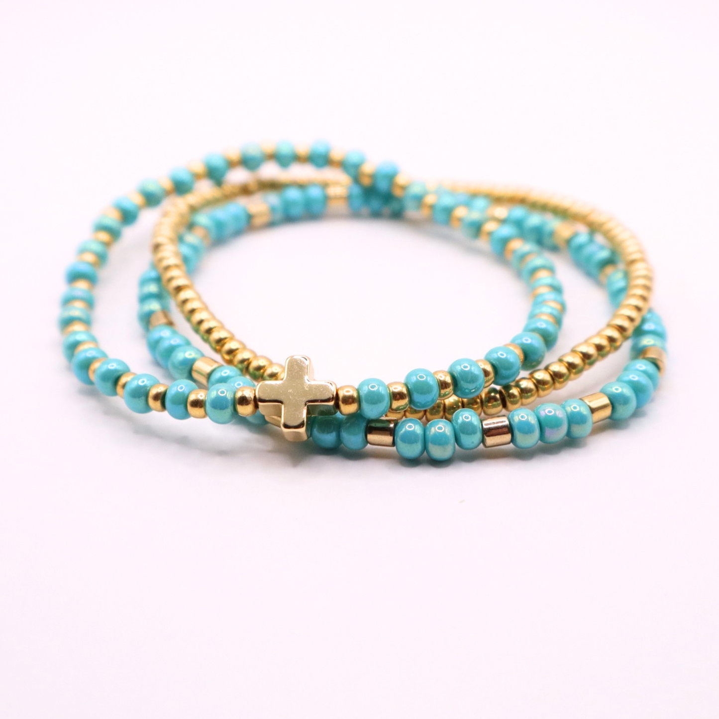 Turquoise beaded bracelet stack with gold accents and a gold cross charm on a white background