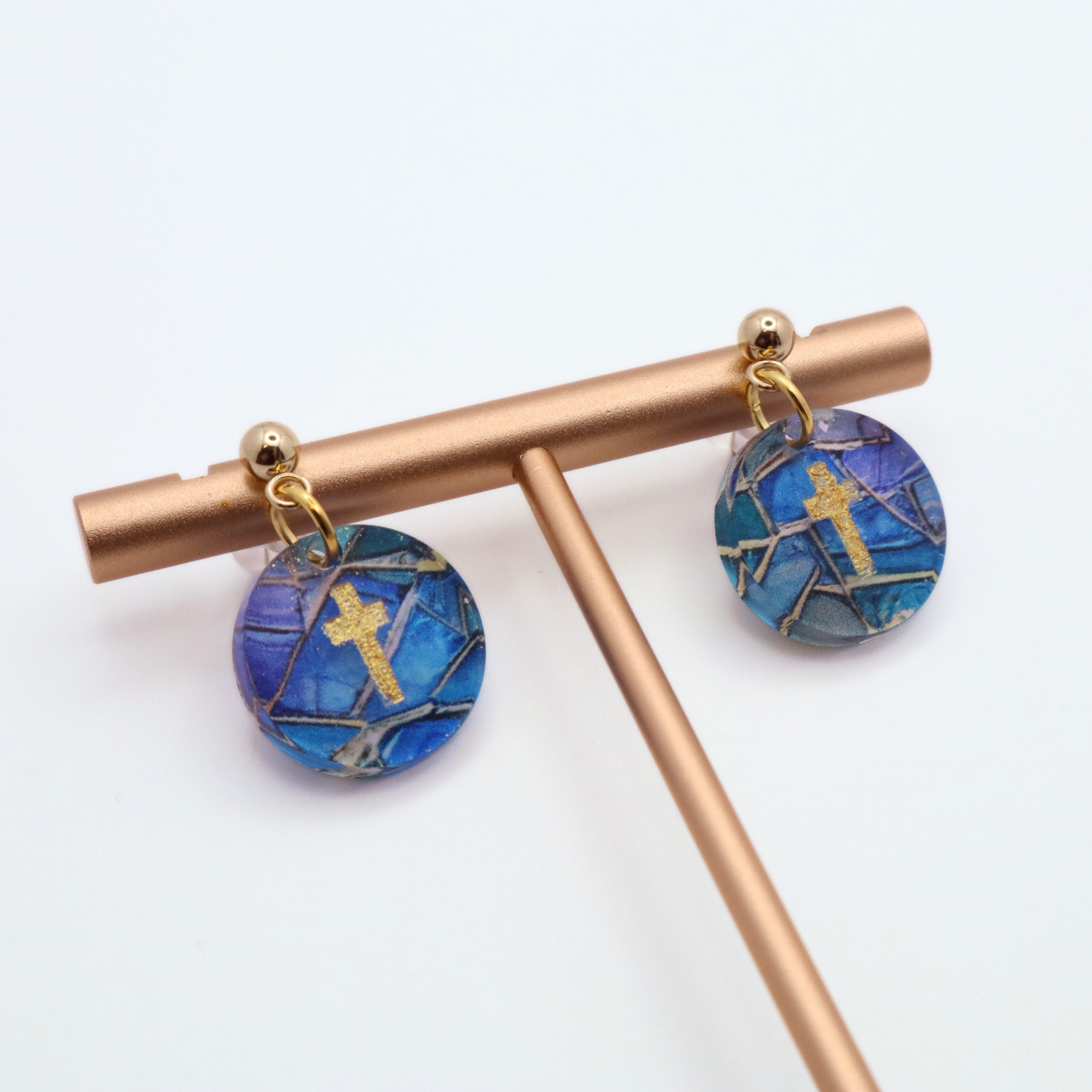 Lightweight christian dangle earrings with blue and purple stained glass design and gold cross accents shown on stainless steel posts