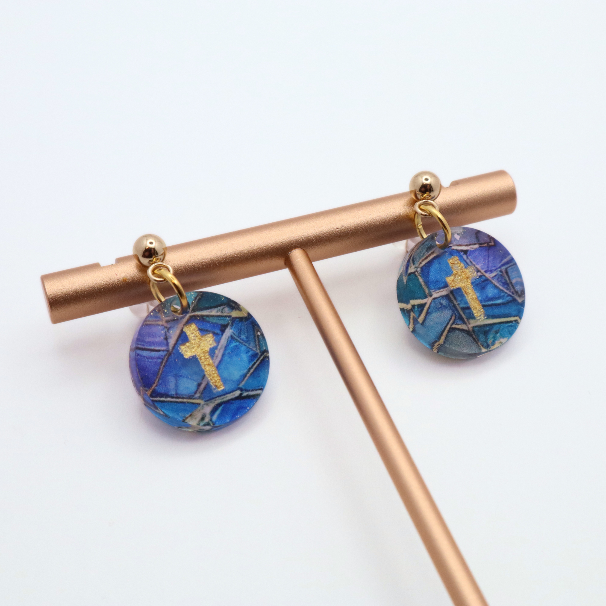 Lightweight christian dangle earrings with blue and purple stained glass design and gold cross accents shown on stainless steel posts