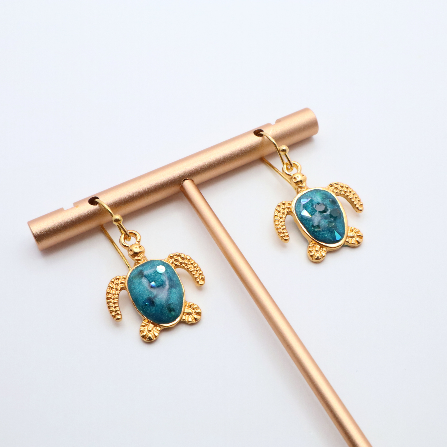 Turtle-shaped earrings with teal blue resin on gold hooks, displayed on a white background.