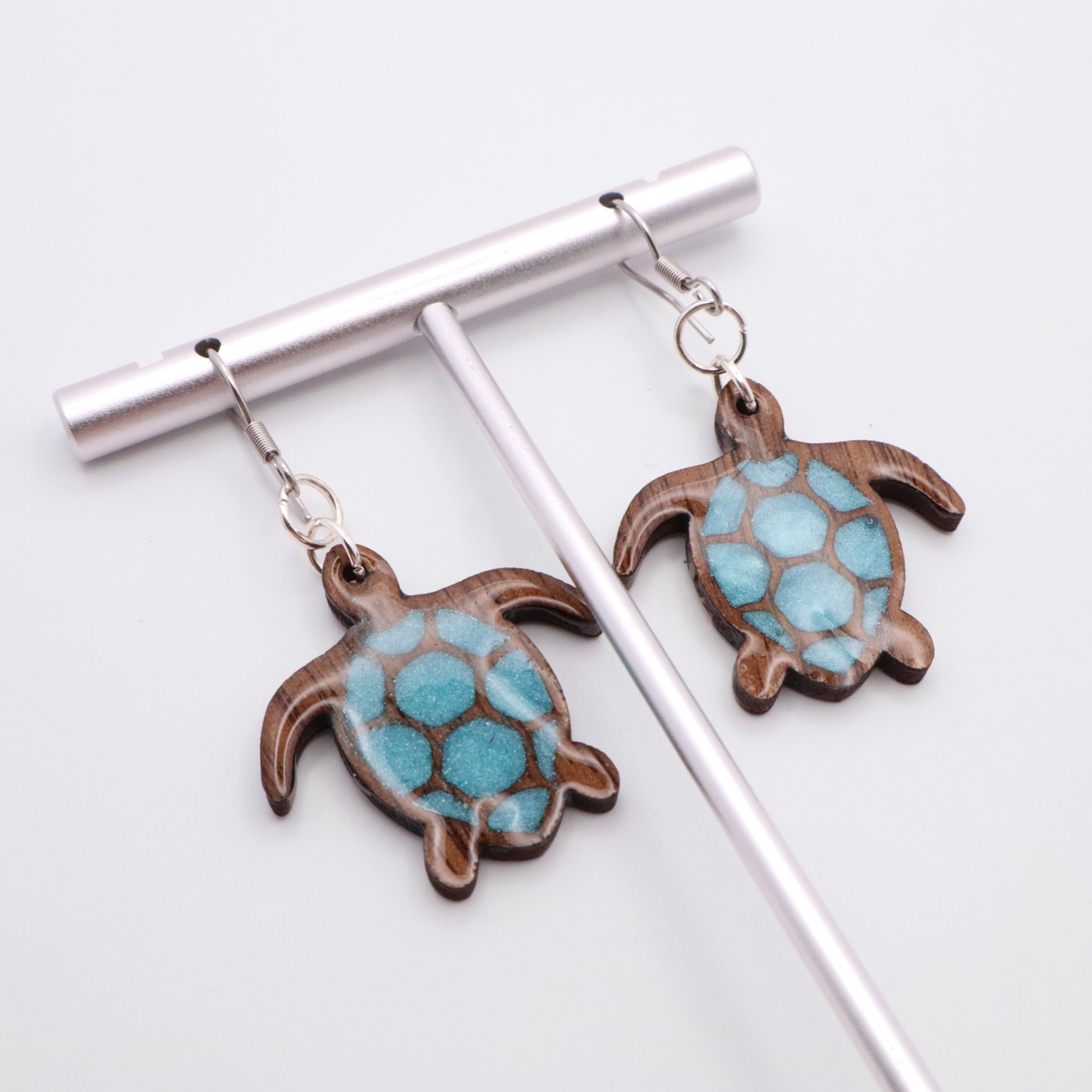 Turtle-shaped black walnut earrings with sea glass blue resin on a white background