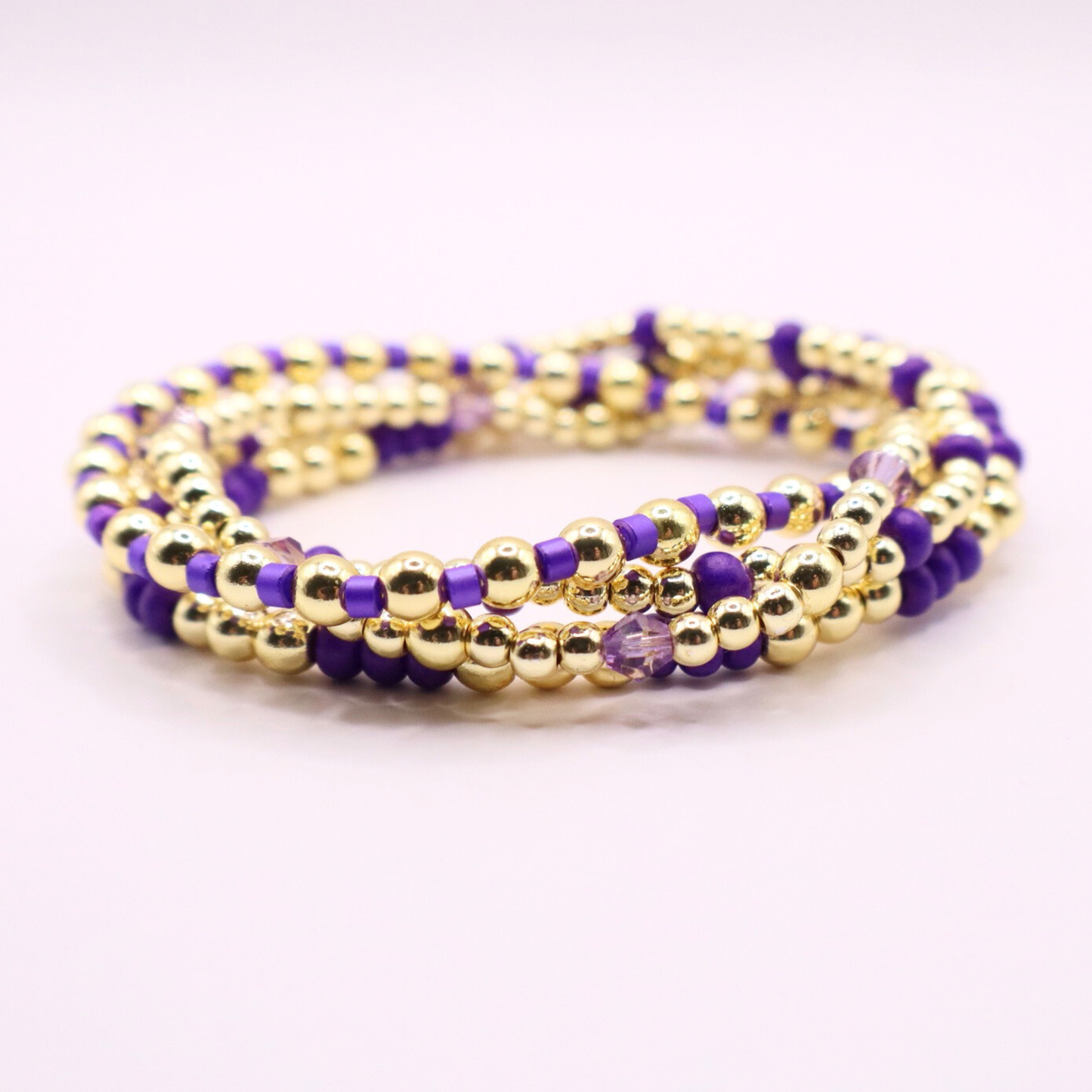 Elegant stack of stretch bracelets featuring rich purple Preciosa seed beads, faceted crystal details, and gold-tone hematite accent beads on a clean white background.