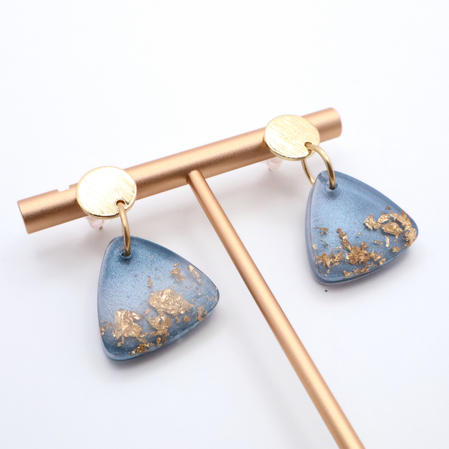 Pair of earrings with blue teardrop-shaped resin with gold accents on a white background