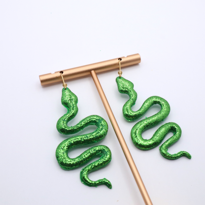 Green glitter snake-shaped earrings on a white background