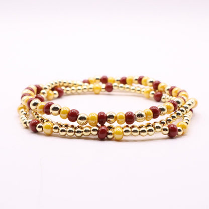 Set of gold and burgundy beaded bracelets on a white surface