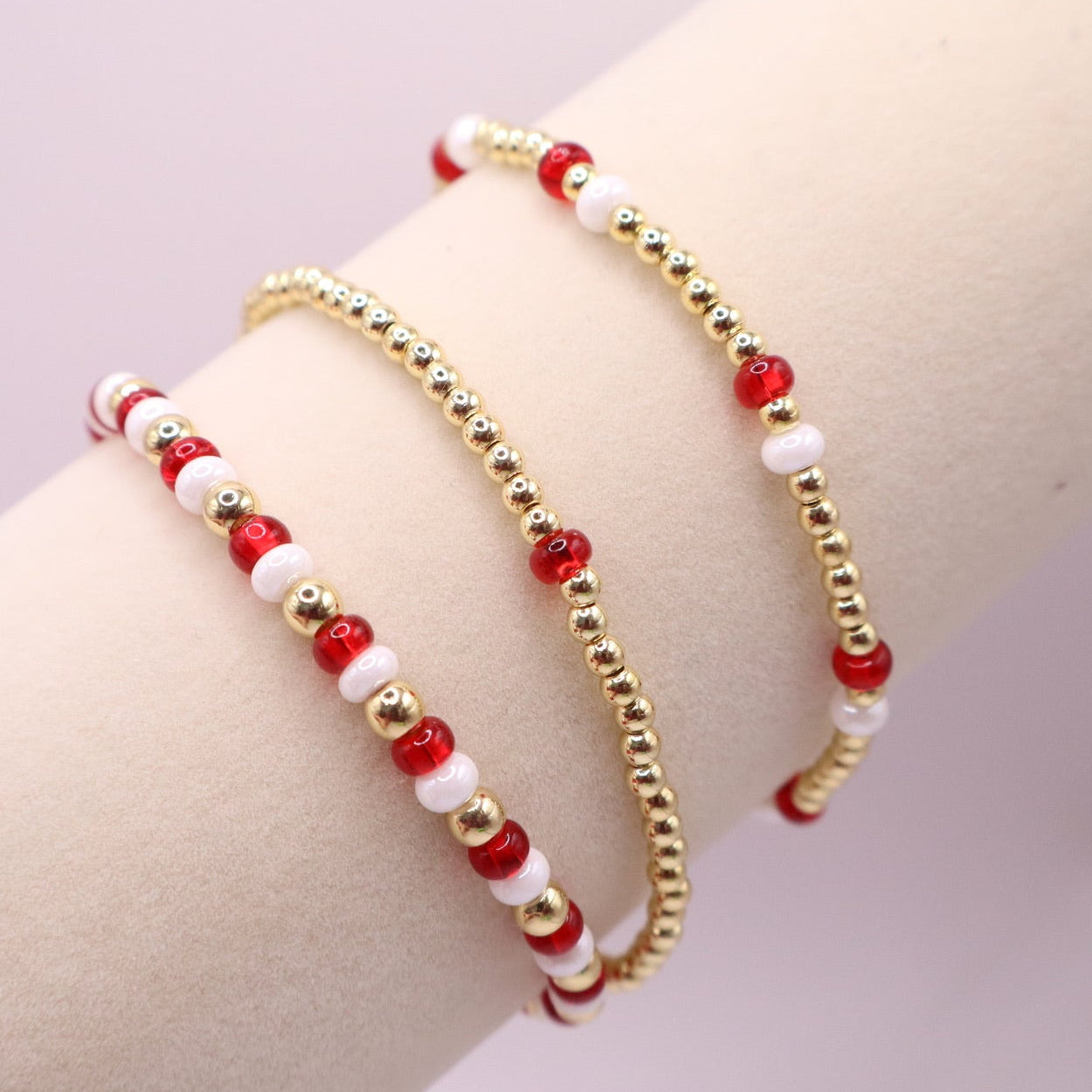 Three beaded bracelets with red, white, and gold accents on a bracelet display against a light background.