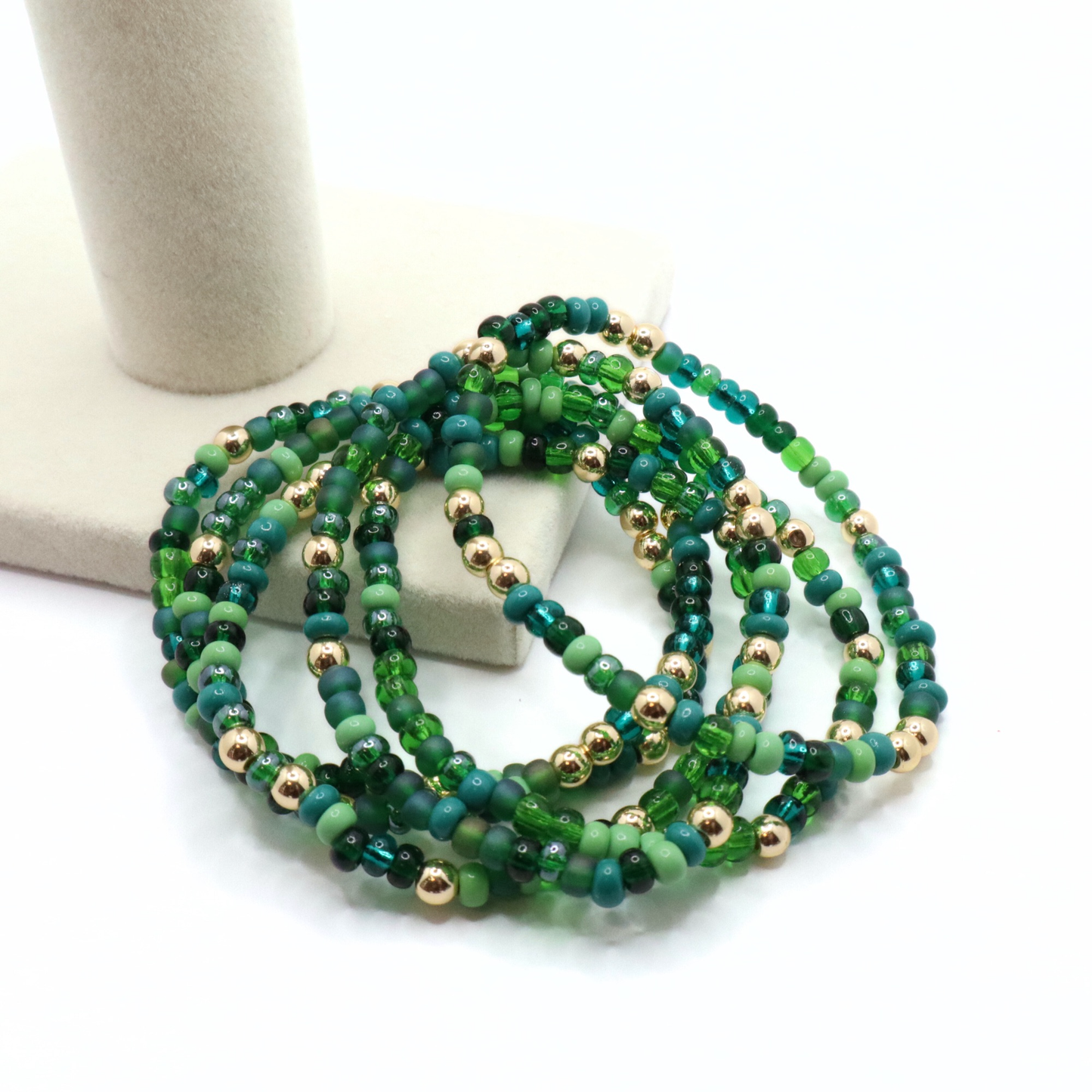 Set of six green beaded bracelets with gold accents on a white surface