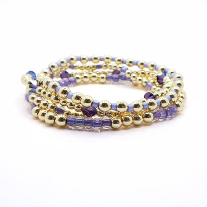 Elegant lavender bracelet stack with gold beads displayed on a wrist jewelry stand.