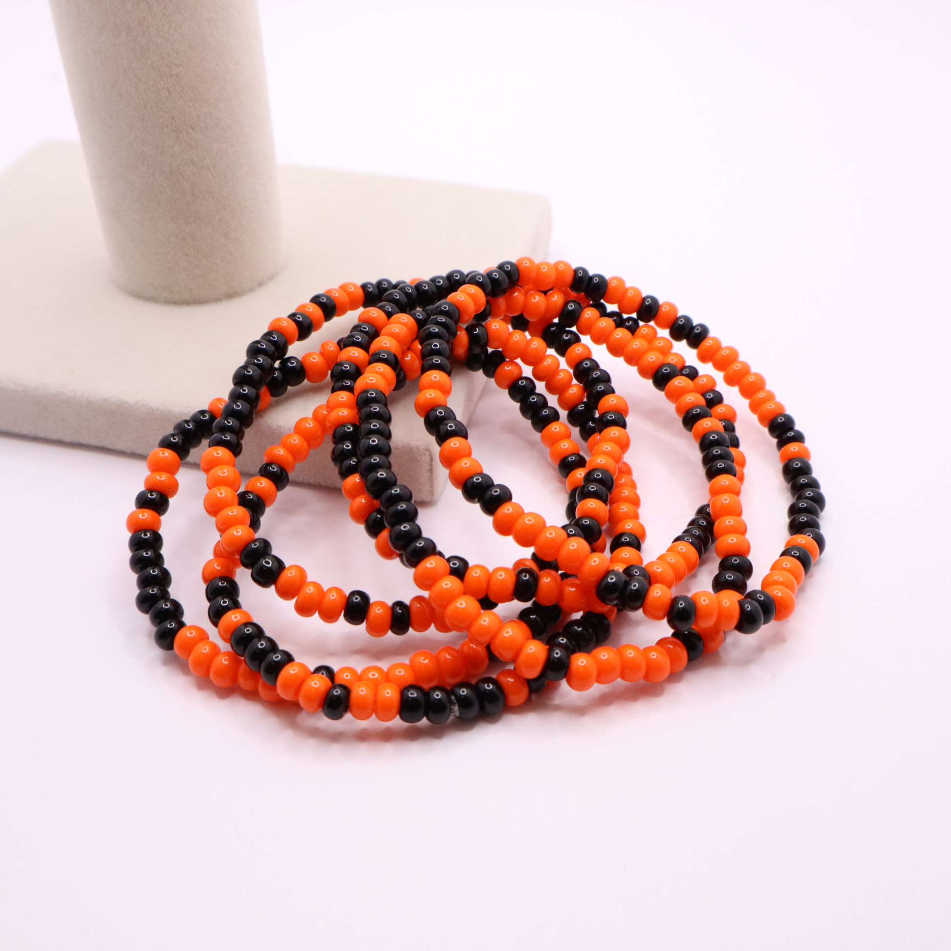 Set of six orange and black seed bead stretch bracelets featuring random orange and black seed beads on a white background