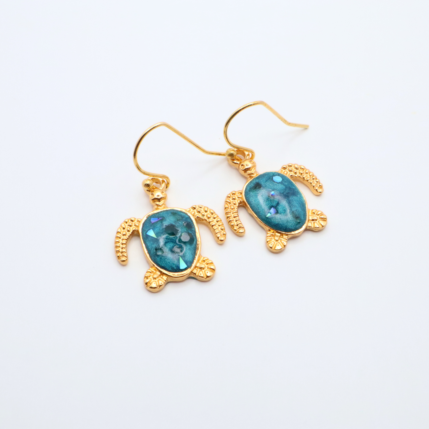 Turtle-shaped earrings with teal blue resin centers and gold frames on a white background