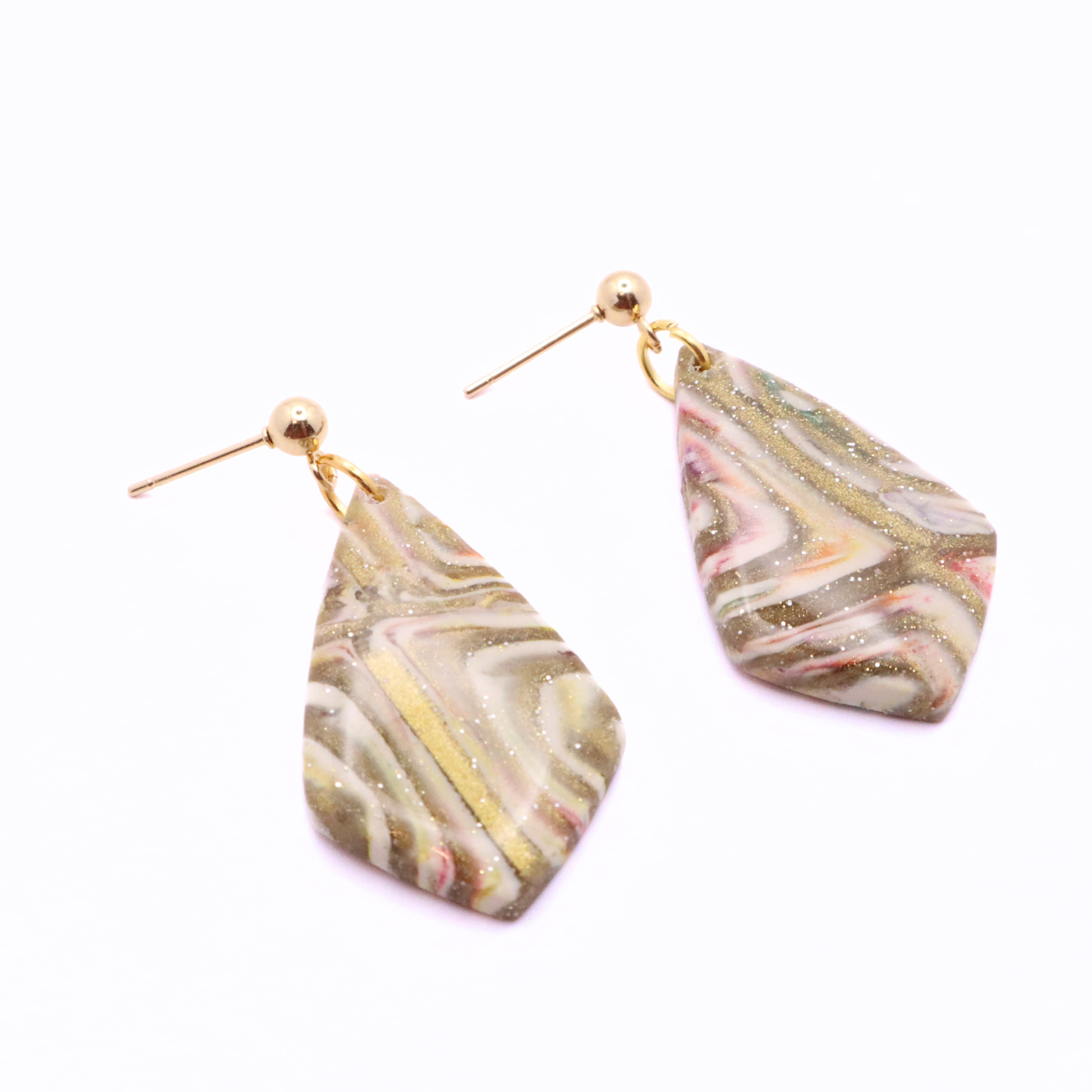 Close-up of polymer clay earrings with marbled beige, white, and blush tones featuring gold shimmer and stainless steel posts
