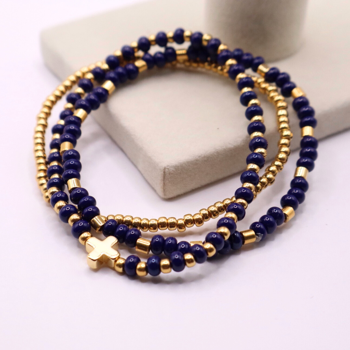 Three navy blue beaded bracelets with gold plated accents on a white surface.