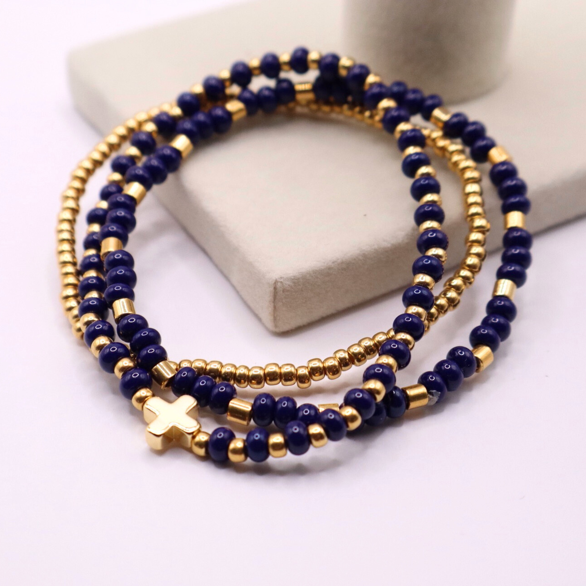 Three navy blue beaded bracelets with gold plated accents on a white surface.
