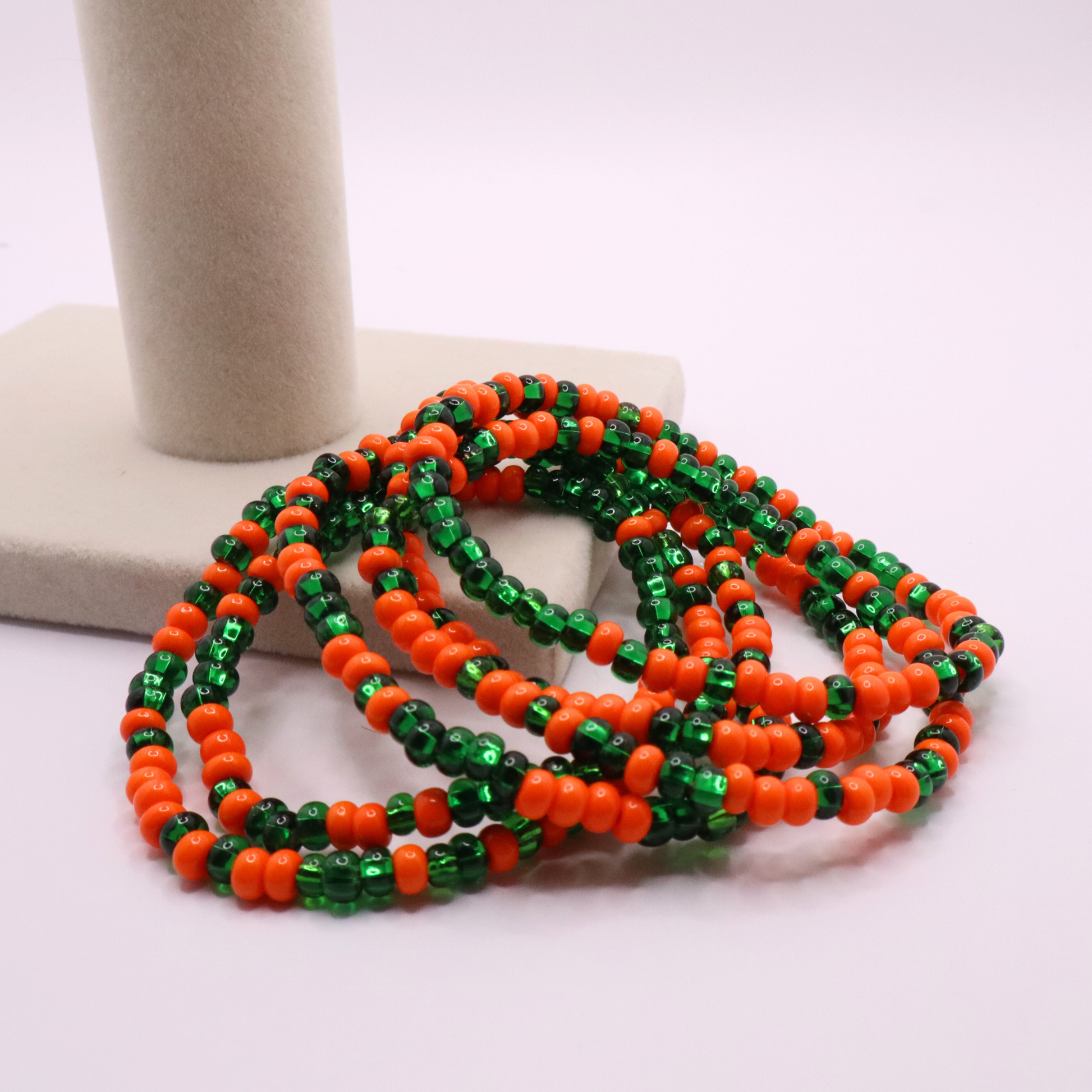 Set of six orange and green seed bead stretch bracelets featuring random orange and green seed beads on a white background