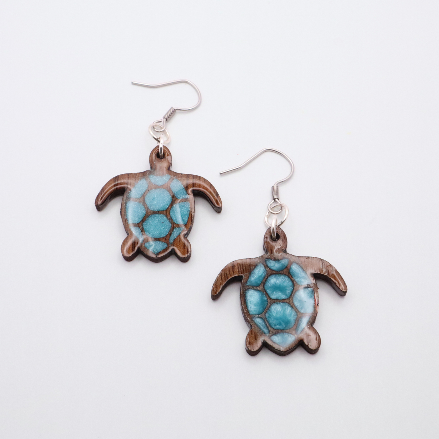 Turtle-shaped black walnut earrings with sea glass blue resin on a white background