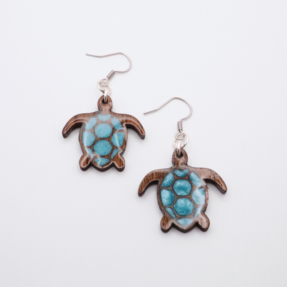 Turtle-shaped black walnut earrings with sea glass blue resin on a white background