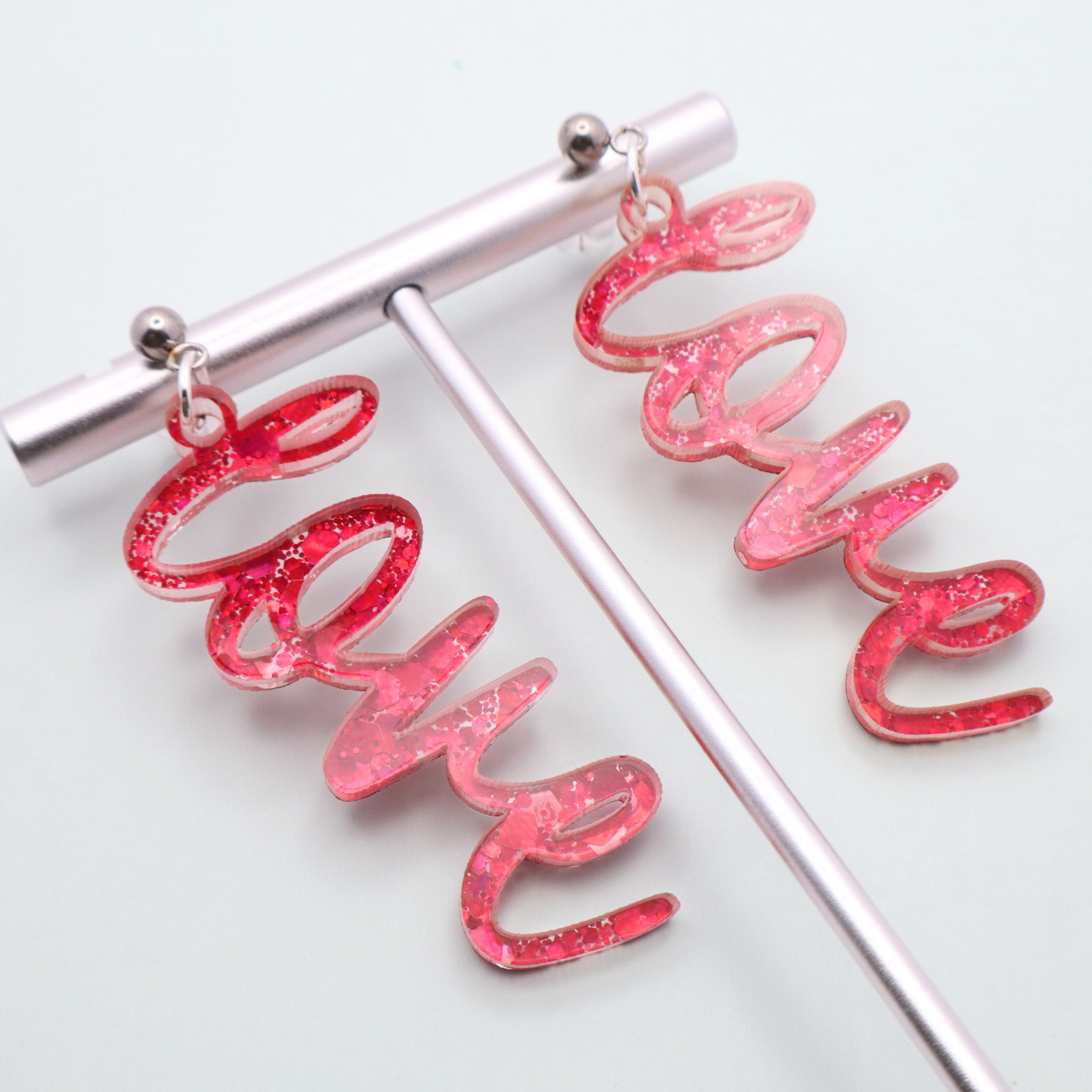 Pink glittery 'love' earrings on a white background
