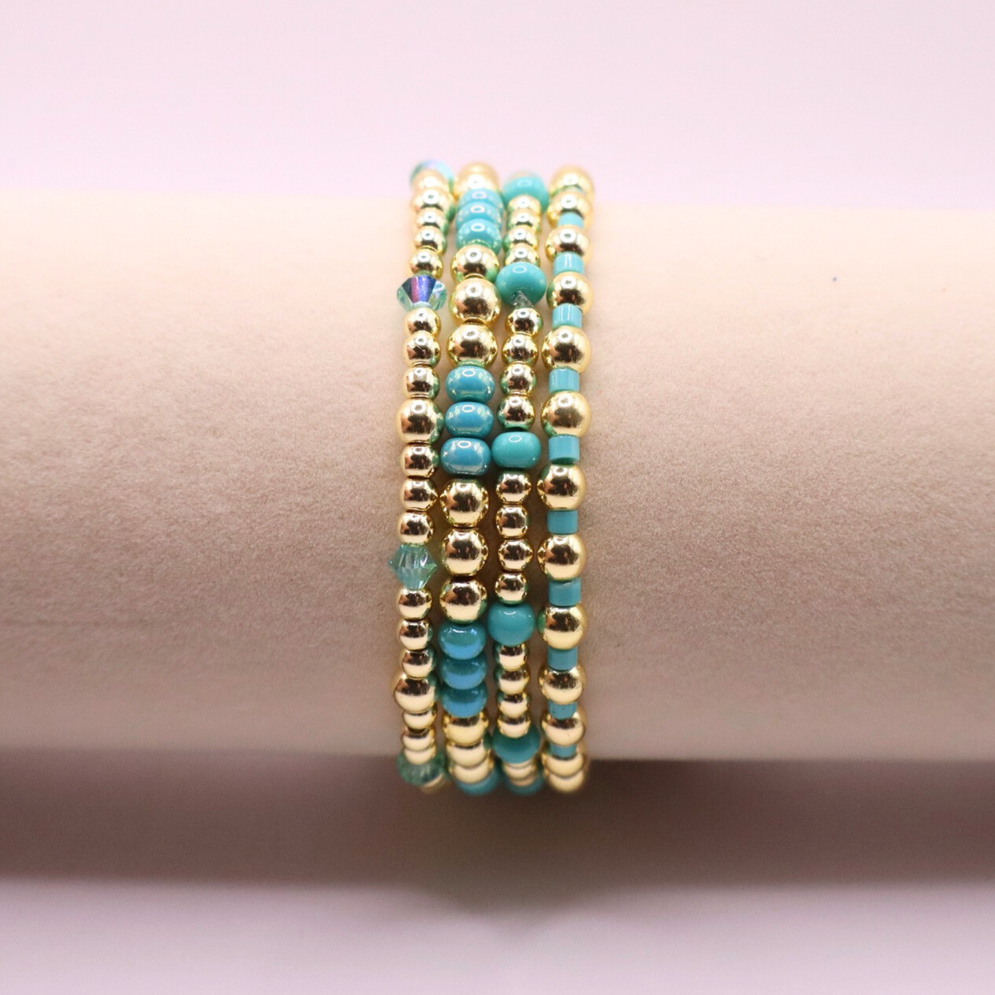 Layered bracelet stack with turquoise Preciosa seed beads, shimmering crystal accents, and gold-tone hematite beads on a clean white background.