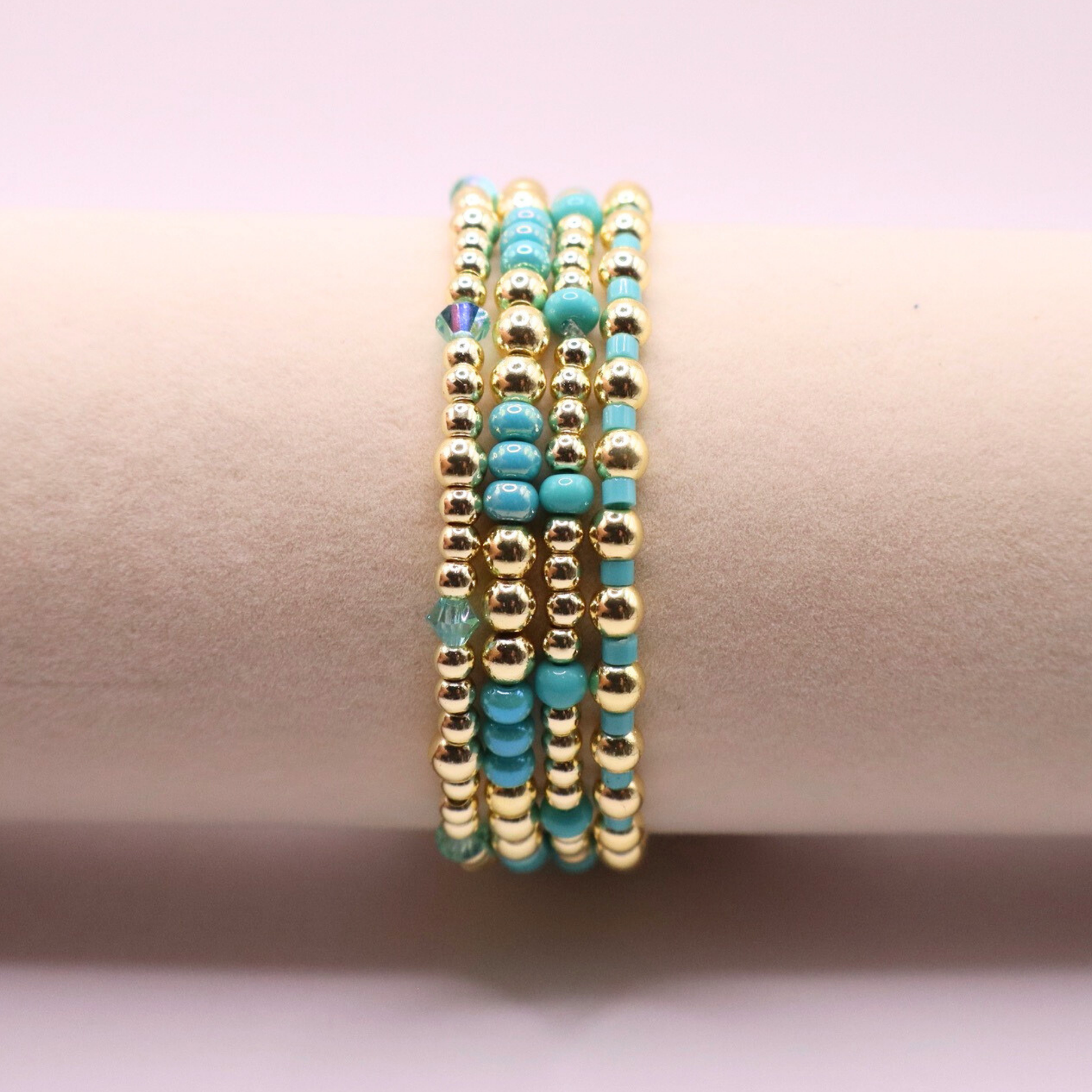 Layered bracelet stack with turquoise Preciosa seed beads, shimmering crystal accents, and gold-tone hematite beads on a clean white background.