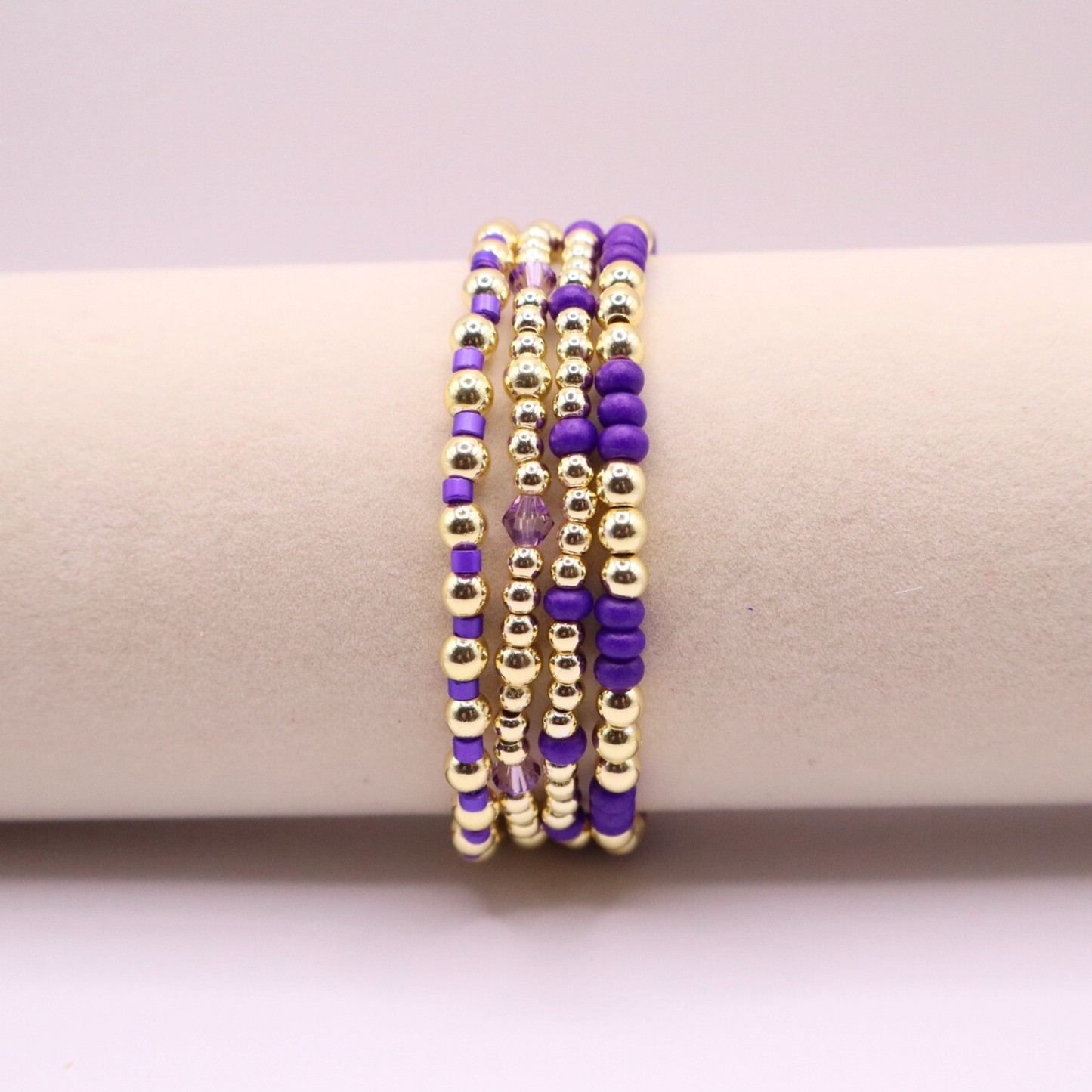 Elegant stack of stretch bracelets featuring rich purple Preciosa seed beads, faceted crystal details, and gold-tone hematite accent beads on a clean white background.